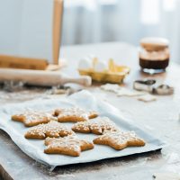 close-up view of delicious ginger cookies on baking tray, cookbook and ingredients on table